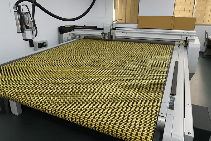 黃色 Kevlar 抗彈布平鋪於數位切割機床台上，準備進行裁切